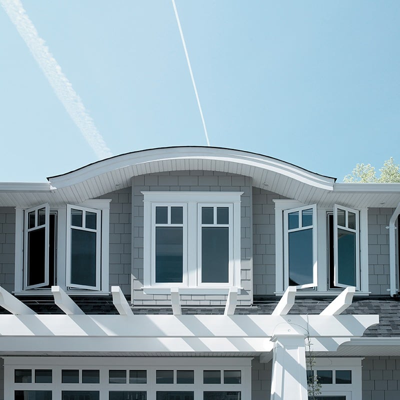 The top story of a beach-style home with closed windows under a curved eave roof and opened windows on either side of it.